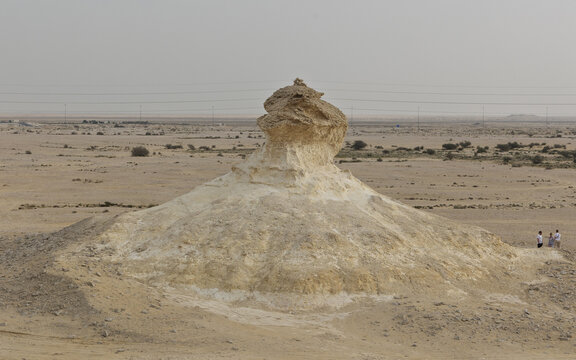 View of Zekreet Rock Formation in the desert landscape with people standing nearby under a clear sky in Zekreet, Al Sheehaniya Municip, Qatar.