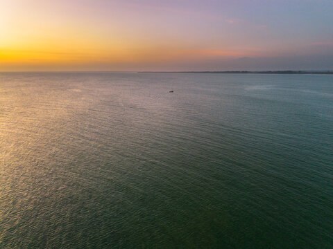 Aerial view of Pantai Panjang Bengkulu at sunset with calm ocean waters and a small boat on the horizon in Kecamatan Ratu Agung, Bengkulu, Indonesia.