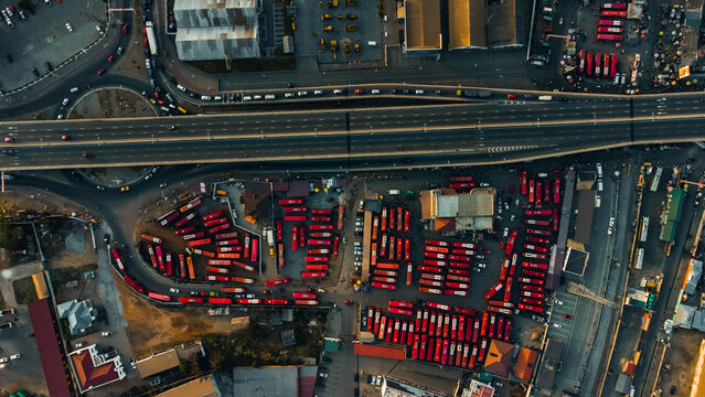Aerial view of VIP Bus Station - JEOUN with rows of red buses parked in an organized lot adjacent to a major highway overpass in Accra, Greater Accra Region, Ghana.