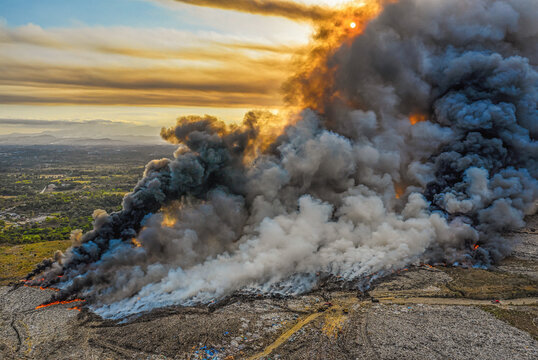 Aerial view of the massive fire at the Vertedero Duquesa landfill with thick plumes of smoke rising into the sky at sunset in Pantoja, Santo Domingo, Dominican Republic.