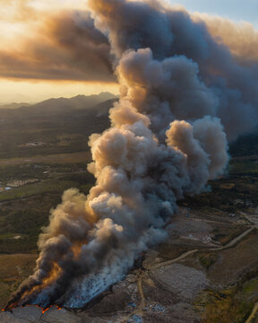 Aerial view of the Vertedero Duquesa landfill fire with thick smoke rising into the sky during golden hour in Pantoja, Santo Domingo, Dominican Republic.