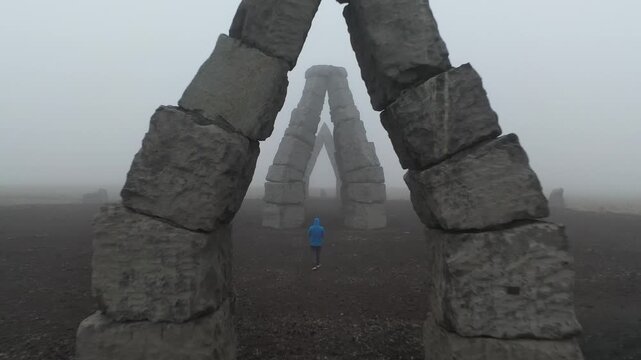 Aerial view of Arctic Henge with a person in a blue jacket standing under stone arches in the mist in Raufarhofn, Nordurthing, Iceland.