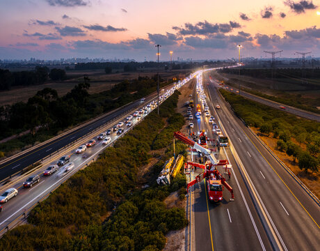 Aerial view of an overturned truck being recovered by a crane on the side of a busy highway during sunset in Rosh Haayin, Center District, Israel.