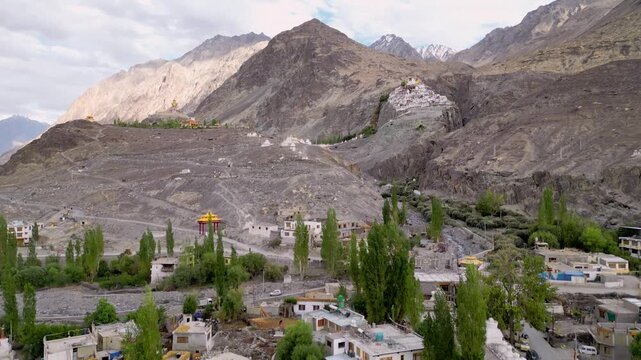 Aerial view of Diskit Monastery perched on a rocky hillside above the village, with lush green trees, houses, and winding roads in Diskit, Ladakh, India.