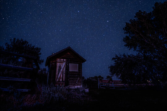 View of a rustic wooden shed under a vast starry night sky in a rural landscape in Picabo, Idaho, United States.