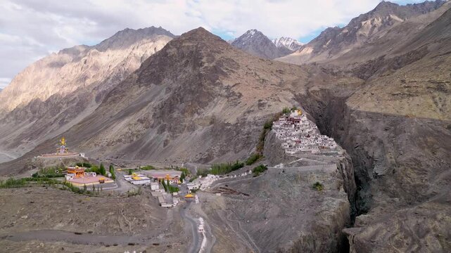 Aerial view of Diskit Monastery nestled in the rugged mountains of the Nubra Valley, featuring traditional white buildings and a golden statue in Diskit, Ladakh, India.