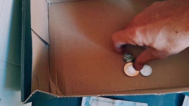 Hand rearranging Brazilian currency coins inside cardboard box motion video footage