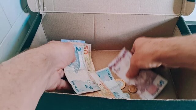 Hands sorting brazilian paper currency inside cardboard box motion clip