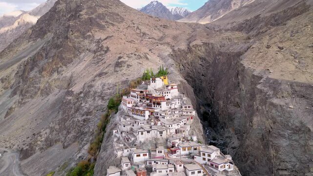 Aerial view of Diskit Monastery with its traditional white buildings perched on a rocky cliff against a rugged mountain backdrop in Diskit, Ladakh, India.