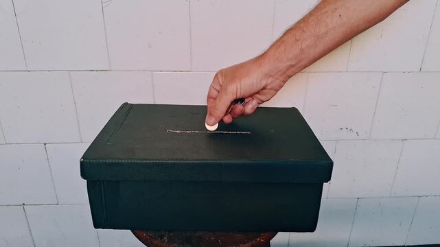 Hand inserting metal coin into donation box motion video footage