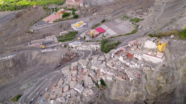 Aerial view of Diskit Monastery perched on a rocky cliff with surrounding traditional buildings and winding roads in Diskit, Ladakh, India.
