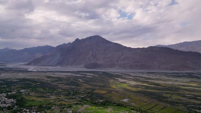 Aerial view of Diskit Monastery nestled in the vast Ladakh valley with rugged mountains and green fields under a cloudy sky in Diskit, Ladakh, INDIA.