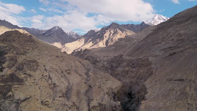 Aerial view of the rugged, arid mountain landscape of the Himalayas with deep valleys and rocky slopes under a blue sky with scattered clouds in Diskit, Ladakh, INDIA.