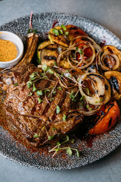 Grilled bone-in steak with vegetables, sauce and microgreens