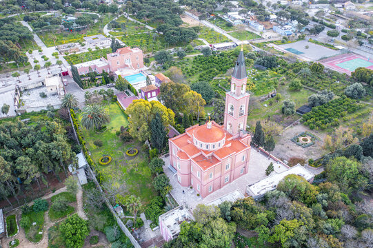 Aerial view of Saint Peter and Saint Tabitha Russian Orthodox Church with its pink walls and red dome, surrounded by lush gardens in Tel Aviv-Yafo, Tel Aviv District, Israel.
