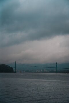 View of the Lions Gate Bridge spanning the water under a cloudy, overcast sky in Vancouver, British Columbia, Canada.