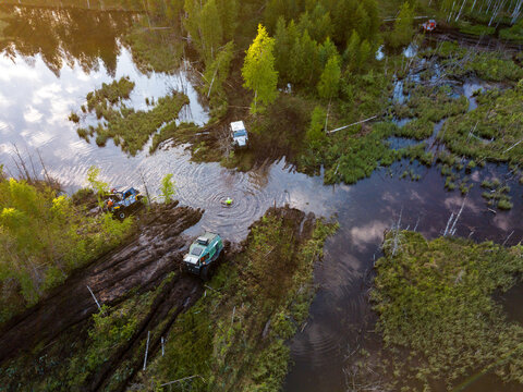 Aerial view of off-road vehicles crossing a marshy area near Lake Ladoga with a person wading in the water surrounded by lush forest in Sortavala, Respublika Kareliya, Russia.