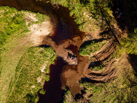 Aerial view of an off-road vehicle crossing a muddy stream surrounded by lush green grass and forest in Sortavala, Respublika Kareliya, Russia.