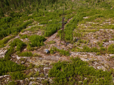 Aerial view of a tall electricity pylon in a rocky, forested landscape near Lake Ladoga with a vehicle and people nearby, Sortavala, Respublika Kareliya, Russia.