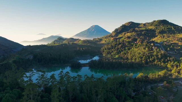 Aerial view of Telaga Warna lake surrounded by lush green hills and volcanic mountains in Kejajar, Central Java, Indonesia.