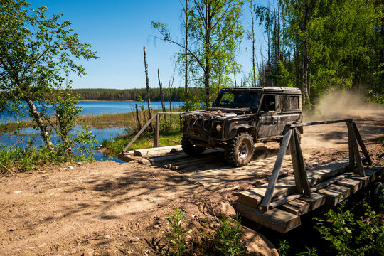 View of a black off-road vehicle crossing a rustic wooden bridge on a dirt path beside the shores of Lake Ladoga in Sortavala, Respublika Kareliya, Russia.
