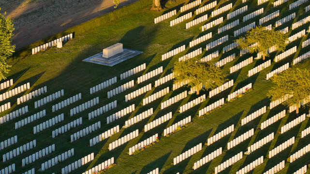 Aerial view of Warlencourt British Cemetery featuring rows of white headstones on manicured green grass with long shadows cast by the sun, Warlencourt-Eaucourt, Hauts-de-France, France.