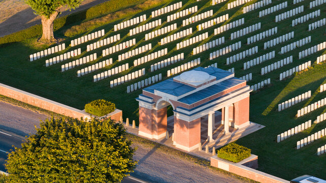 Aerial view of Warlencourt British Cemetery with rows of white headstones, a brick entrance structure, and surrounding green grass in Warlencourt-Eaucourt, Hauts-de-France, France.
