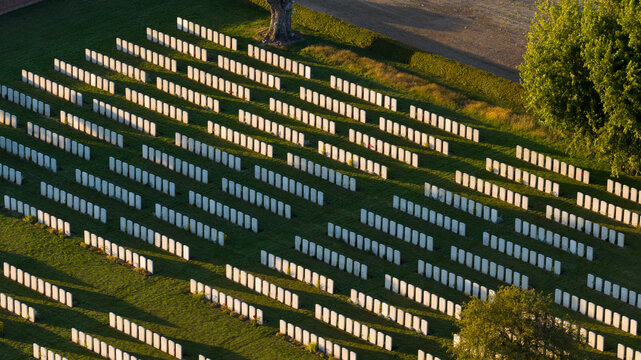 Aerial view of Warlencourt British Cemetery with rows of white headstones set in green grass, trees, and shadows in Warlencourt-Eaucourt, Hauts-de-France, France.