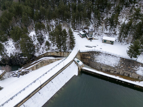 Aerial view of hydroelectric power plant dam surrounded by snow-covered pine forests and mountain terrain in Val d'Aran, Catalonia, Spain.
