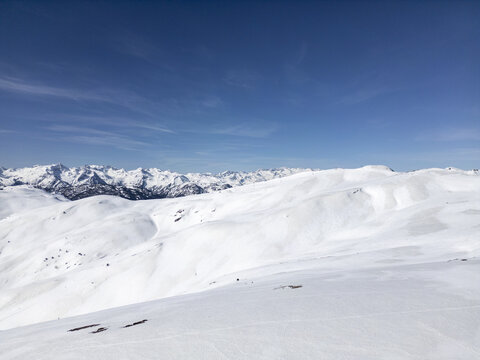 Aerial view of the Baqueira ski resort featuring vast snow-covered slopes and rugged mountain peaks under a clear blue sky in Baqueira, Cataluna, Spain.