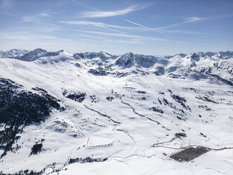 Aerial view of the Baqueira ski resort featuring expansive snow-covered mountain slopes, ski runs, and a parking area under a clear blue sky in Baqueira, Cataluna, Spain.