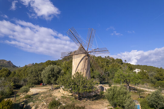 Aerial view of Molino de Sa Planeta surrounded by lush greenery and rolling hills under a bright blue sky in Andratx, Balearic Islands, Spain.
