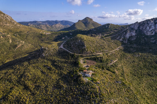 Aerial view of Coll de sa Gran Mola surrounded by rugged hills, winding dirt roads, and Mediterranean scrubland under a clear blue sky in Illes Balears, Illes Balears, Spain.