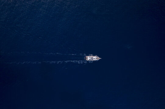 Aerial view of a small boat sailing through the deep blue waters near Port de Sa Dragonera, Islas Baleares, Spain.