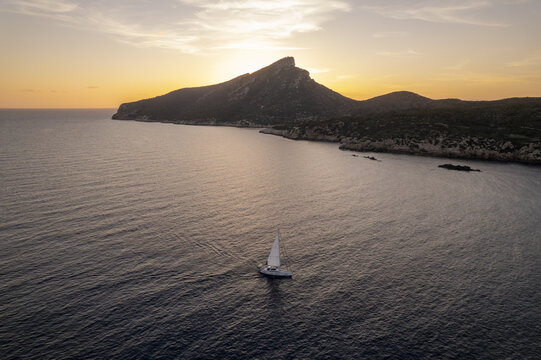Aerial view of a sailboat sailing near the coast of Sa Dragonera island during a golden sunset in Islas Baleares, Spain.