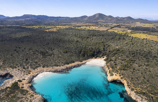 Aerial view of Cala Varques with turquoise waters, rocky cliffs, and Mediterranean scrubland in Mallorca, Spain.