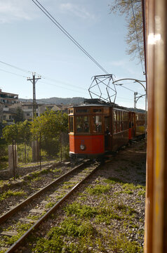 Port de Soller, Spain - 01 April 2018: View of the historic wooden tram at the Estacio de Tramvia with lush greenery and buildings in the background under a clear blue sky.