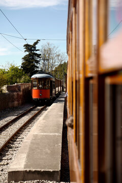 Port de Soller, Illes Balears, Spain - 01 April 2018: View of the historic wooden tram arriving at the Estacio de Tramvia station on a sunny day with lush trees in the background.