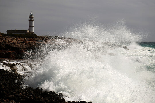 View of the lighthouse at Cap de Ses Salines with powerful waves crashing against the rocky coastline in Mallorca, Balearic Islands, Spain.