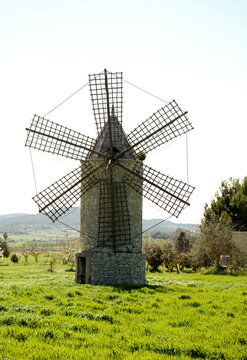 View of a traditional stone windmill standing in a vibrant green field in Mallorca, Balearic Islands, Spain.
