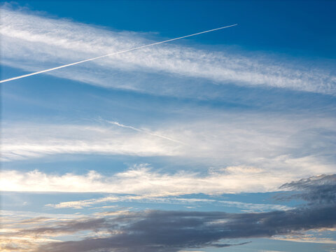 Aerial view of a bright blue sky filled with wispy cirrus clouds and a long white contrail left by an airplane over Cascais, Lisboa, Portugal.