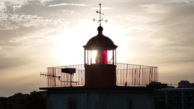Aerial view of the Farol Museu de Santa Marta lighthouse with its red lantern room and weather vane silhouetted against the sunset sky in Cascais, Lisboa, Portugal.