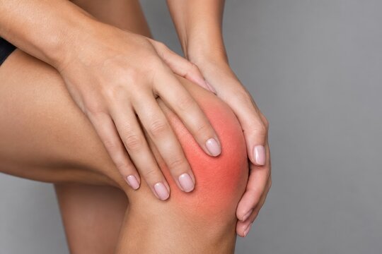 Nahaufnahme einer Frau, die ihr schmerzendes Knie h&auml;lt. Ein roter Bereich markiert den Schmerz am Gelenk. Konzept f&uuml;r Gelenkschmerzen, Arthritis und Sportverletzungen