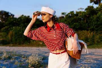 Young woman wearing sailor hat and striped shirt looking through binoculars on sunny beach. The theme is maritime lifestyle and adventure during a warm summer vacation day. © SHOTPRIME STUDIO