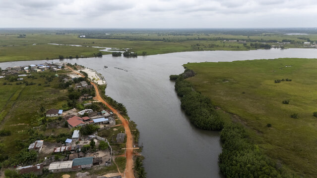 Aerial view of Gogotinkpon village situated along a river with a dirt road and lush green vegetation in Kpomasse, Mono, Benin.