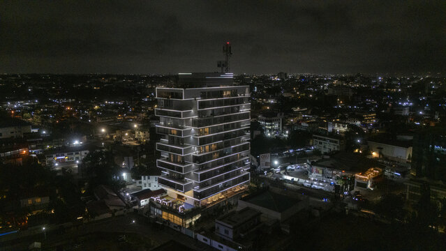 Aerial view of a modern high-rise building illuminated with LED lights at night, surrounded by the urban cityscape of Accra, Greater Accra Region, Ghana.