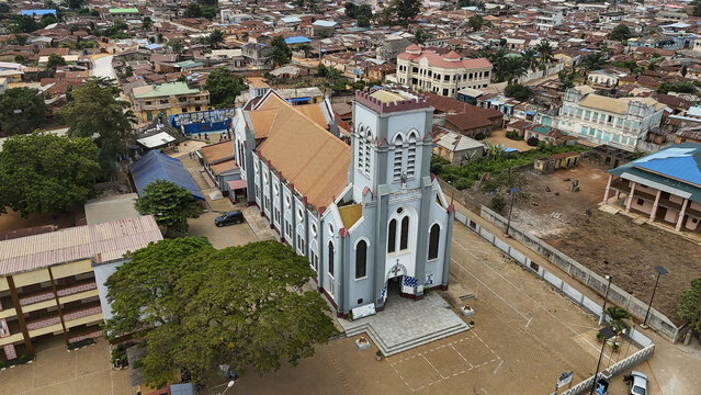 Aerial view of the Basilica of the Immaculate Conception surrounded by the dense urban landscape and rooftops of Ouidah, Atlantique, Benin.