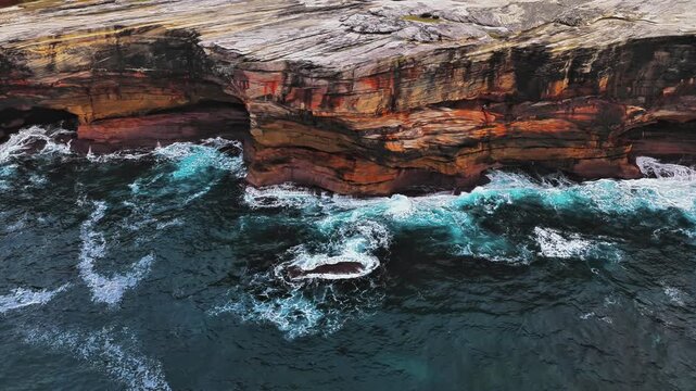 Aerial view of rugged coastal cliffs with crashing waves and turquoise water at Kurnell, New South Wales, Australia.