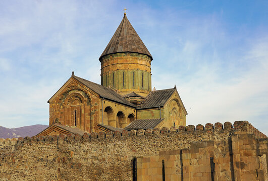 The historic Svetitskhoveli Cathedral and its surrounding defensive stone walls stand under a partly cloudy sky in Mtskheta, Georgia