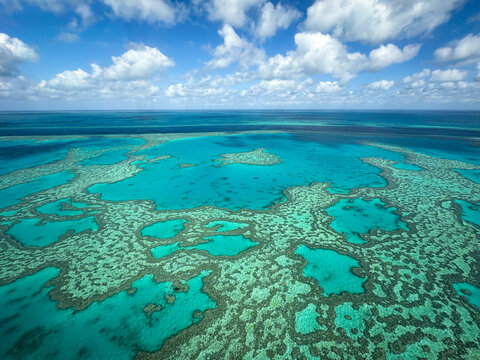 Aerial view of the Great Barrier Reef featuring vibrant turquoise coral formations and deep blue waters under a bright sky near Airlie Beach, Queensland, Australia.